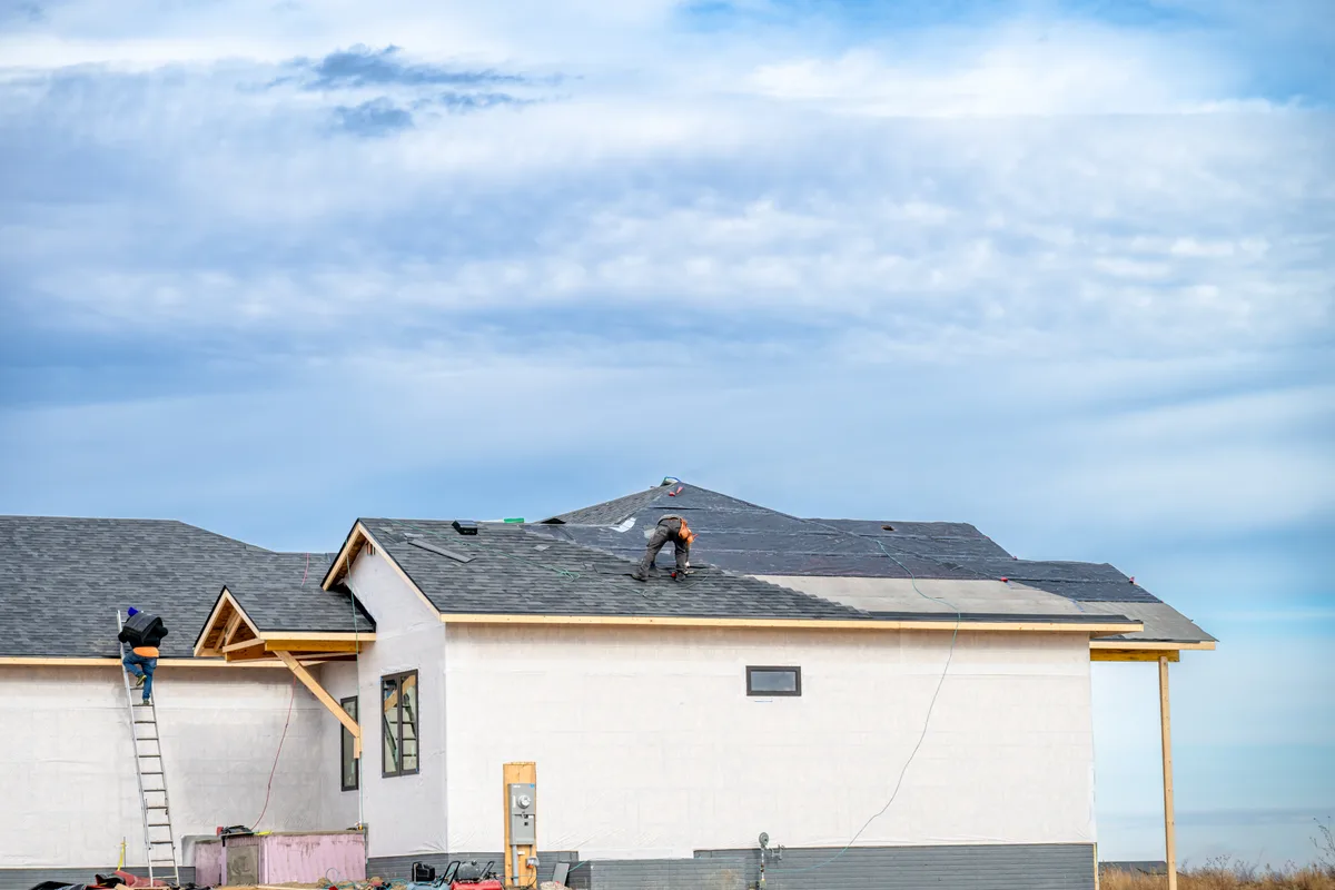 House under construction with workers on roof — nonwoven house wrap and roofing underlay application